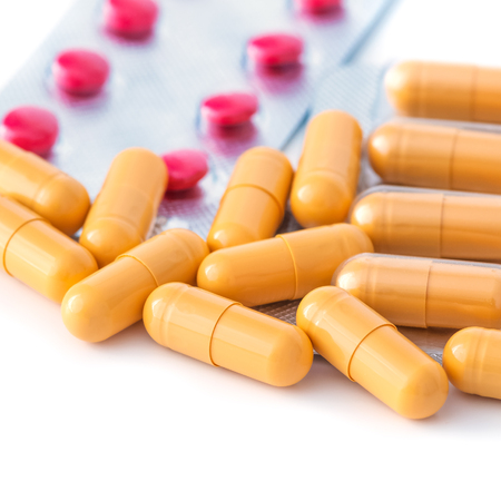 Red and yellow tablets and blisters scattered on a white background