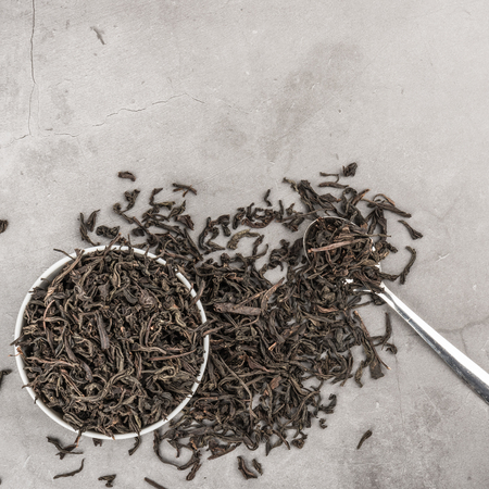 Dried tea in a white ceramic cup with a spoon on a gray textured background. View from above. Layoutの写真素材