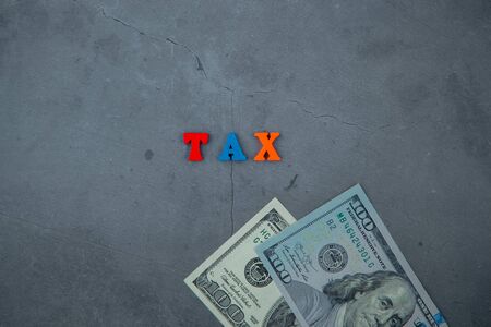 The multicolored tax word is made of wooden letters on a grey plastered wall background.