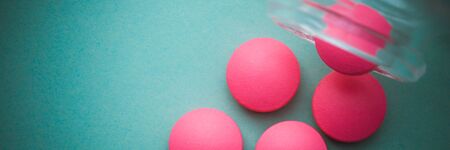 Pink tablets are poured from a glass jar on a green background.の写真素材