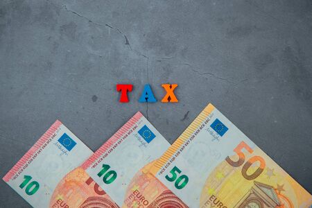 The multicolored tax word is made of wooden letters on a grey plastered wall background.の写真素材