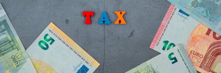 The multicolored tax word is made of wooden letters on a grey plastered wall backgroundの写真素材