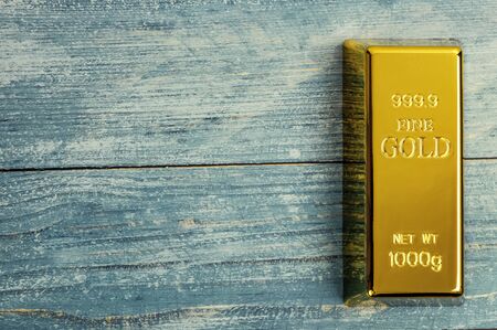 Ingot of pure gold metal bullion on a background of blue wooden boards