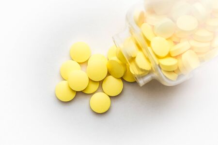 Yellow pills scattered from a glass jar on a white backgroundの写真素材