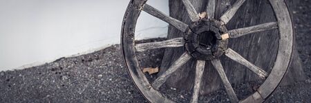 An old wooden cartwheel stands at the wall of the house
