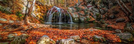 Waterfall in the forest in autumn among the fallen colorful bright leavesの写真素材