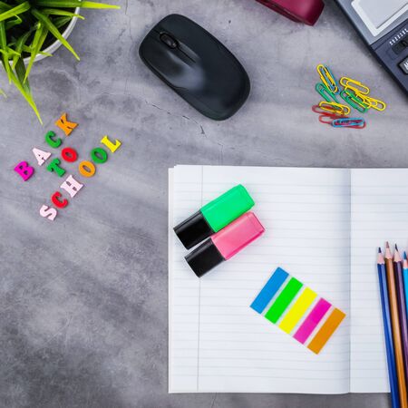 The layout of school supplies on a dark gray background. Top view, the sun's rays from the side....