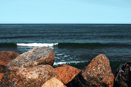 Large stones lie on the beach in front of the wavesの写真素材