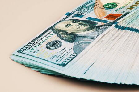 A pack of dollars. A large wad of hundred-dollar bills is lying on a beige background. the wad is...