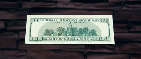 A hundred-dollar bill. Close-up, against a brick wall of dark red brown color.