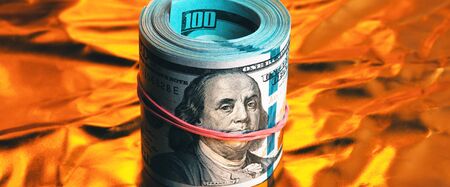 A roll of one hundred American dollars in close-up on a burning bright gold background. Close-up, full-contrast color image. Free space for labels and text.の写真素材