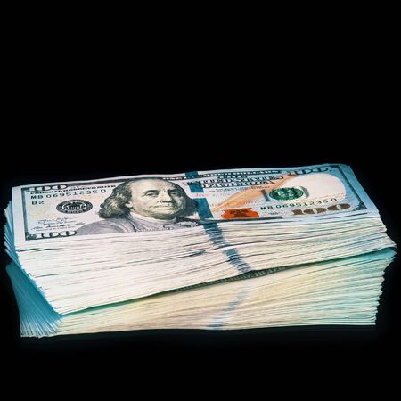 Isolated bundle of dollars. A large stack of hundred-dollar bills lies on a black backgroundの写真素材