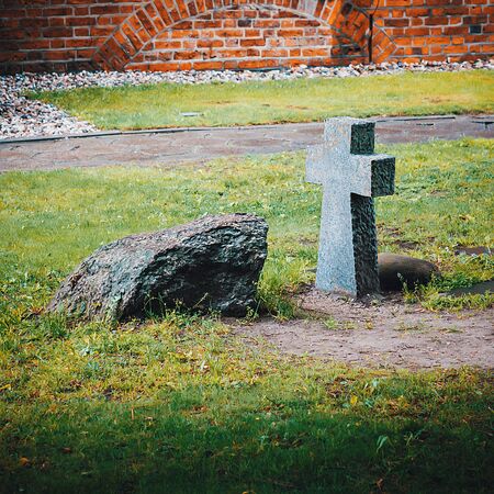 An ancient stone funeral cross and a tombstone on the burial ground near the wall of the old castle.の写真素材