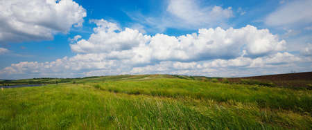 Summer natural landscape, meadow, field, hills. Beautiful blue sky with clouds.の写真素材