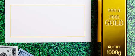 An ingot of gold metal ingot glittering on the grass background and a card for the inscription.の写真素材