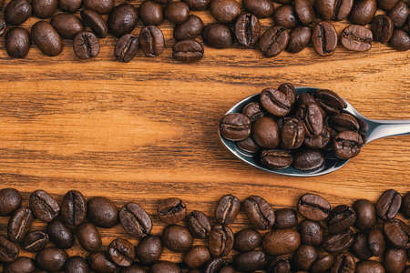 Coffee beans with a spoon close-up scattered on a table made of textured wooden boards.の写真素材