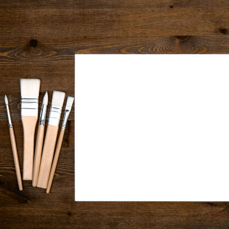 A clean white sheet and brushes on a wood textured background with space to copy.の写真素材