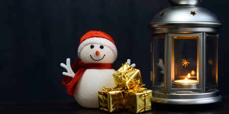 Christmas card: a snowman, a lantern with candles, bright shiny boxes with gifts on a dark background.の写真素材