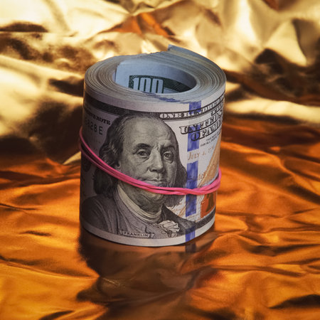 A roll of one hundred American dollars in close-up on a gold background. A big pile of cash dollars....