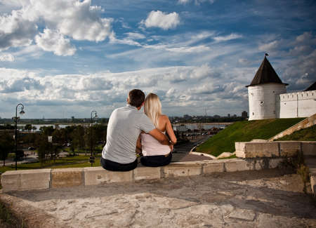 boy and girl sitting on the edge of the wall with his back to the photographerの写真素材