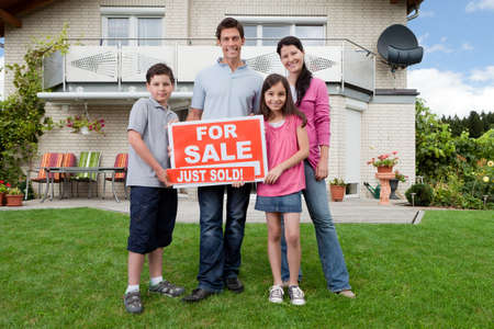 Young happy family holding sold sign outside their new houseの写真素材