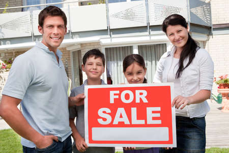 Portrait of young family selling their home holding for sale sign - Outdoorsの写真素材