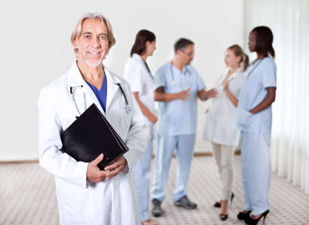 Mature doctor holding files with a group of doctors discussing behindの写真素材
