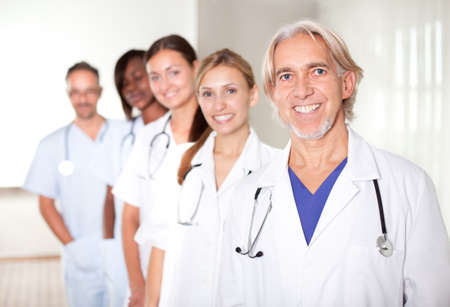 Mature male doctor with his team of colleagues out of focus behind him.の写真素材