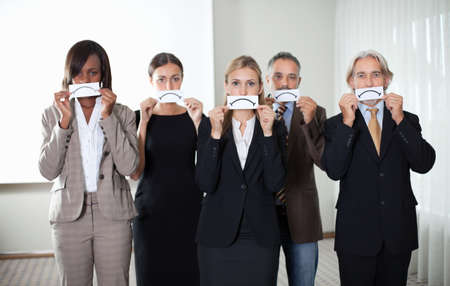 Diverse group of business people holding a card with sad sign by their faces.の写真素材