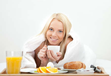Beautiful woman drinking coffee in bedの写真素材