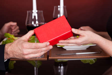 Man giving present to a woman at romantic dinner in restaurantの写真素材