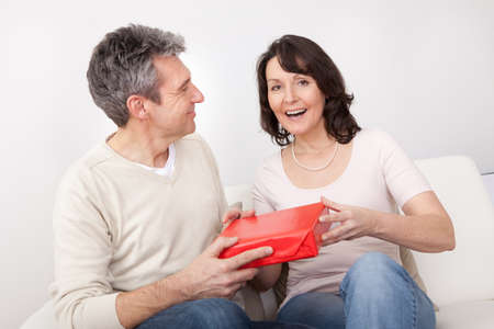 Mature man giving a present to his woman at homeの写真素材