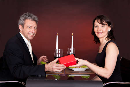 Man giving present to a woman at romantic dinner in restaurantの写真素材