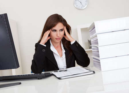 Frustrated businesswoman with stack of folders on computer deskの写真素材