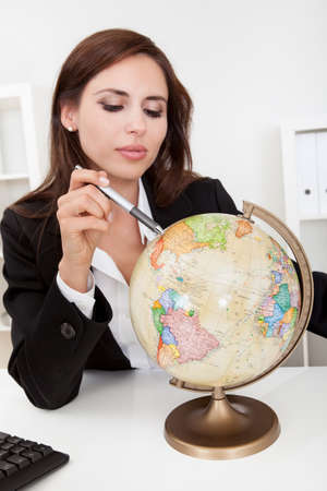 Portrait of a young businesswoman pointing at globe in officeの写真素材