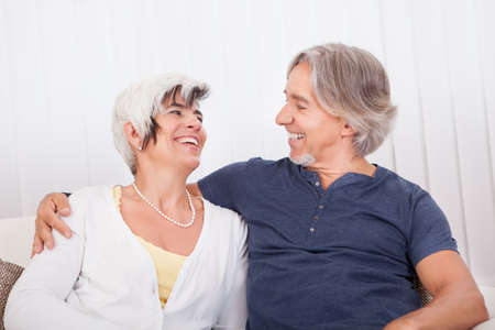 Happy smiling senior couple sitting in a close embrace beaming with vitality and enjoyment of their...