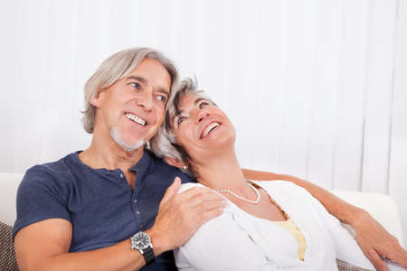 Happy smiling senior couple sitting in a close embrace beaming with vitality and enjoyment of their...