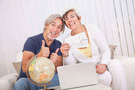 Ecstatic senior couple giving a thumbs up of success and victory as they display the tickets for...