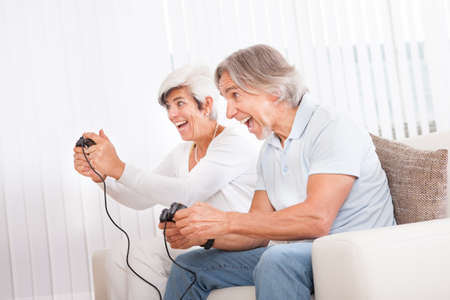 Excited middle-aged couple sitting on a sofa in their living room in front of the television screen...
