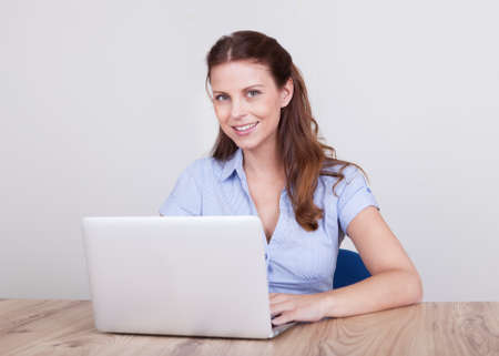 Friendly smiling woman sitting at a wooden table working at a laptopの写真素材