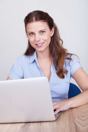 Friendly smiling woman sitting at a wooden table working at a laptopの写真素材