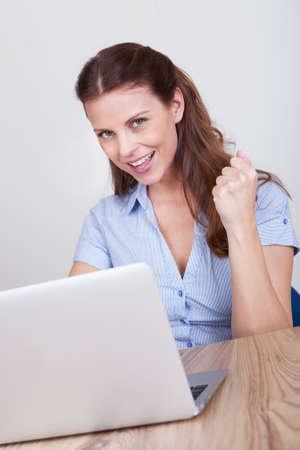 Upbeat successful young woman sitting at her laptop making a fist of jubilation and celebrationの写真素材
