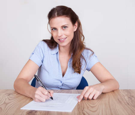 Woman sitting writing on a sheet of paper at a wooden table with distinctive grainの写真素材
