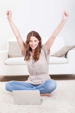 Portrait of an attractive young female sitting on the carpet using a laptopの写真素材
