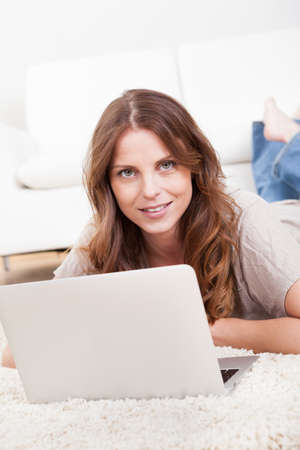 Portrait of an attractive young female sitting on the carpet using a laptopの写真素材