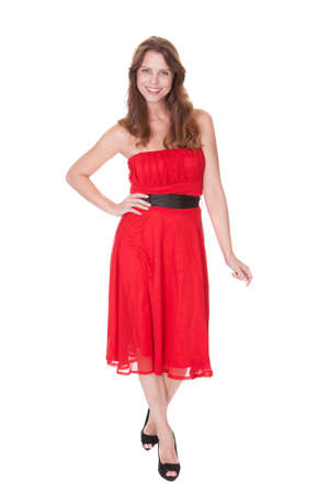 Glamorous elegant woman in a trendy red dress walking towards the camera with a lovely smile isolated on whiteの写真素材