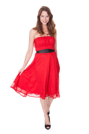 Glamorous elegant woman in a trendy red dress walking towards the camera with a lovely smile isolated on whiteの写真素材