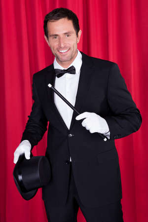 A Magician In A Black Suit Holding An Empty Top Hat And Magic Wand