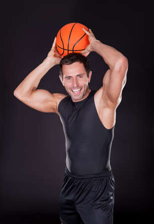 Young Man Throwing Basketball Isolated On Black Backgroundの写真素材
