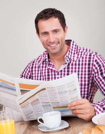 Portrait Of Young Man Reading Newspaper At Breakfast, Indoorsの写真素材
